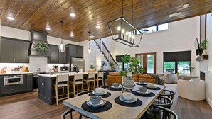 A modern kitchen with dark cabinets, a wooden ceiling, and a dining area with a long table set for four.