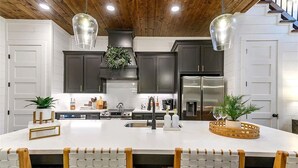 A modern kitchen with dark cabinets, a large island, stainless steel appliances, and pendant lighting.