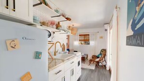 Una cocina compacta con armarios blancos, encimera de mármol y un tendedero sobre el fregadero.