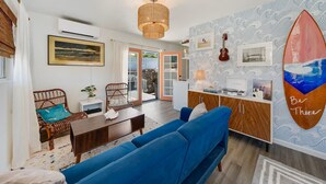 Una sala de estar moderna con un sofá azul, sillas de mimbre, una mesa de comedor y una zona de cocina.