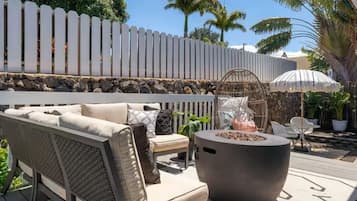 Une terrasse extérieure avec un canapé, des chaises, un foyer et une clôture blanche en bois.