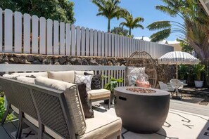 An outdoor patio with a sofa, chairs, a fire pit, and a white picket fence.