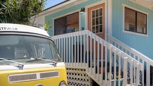 Un auto amarillo antiguo estacionado frente a una casa colorida con un porche blanco y una escalera.