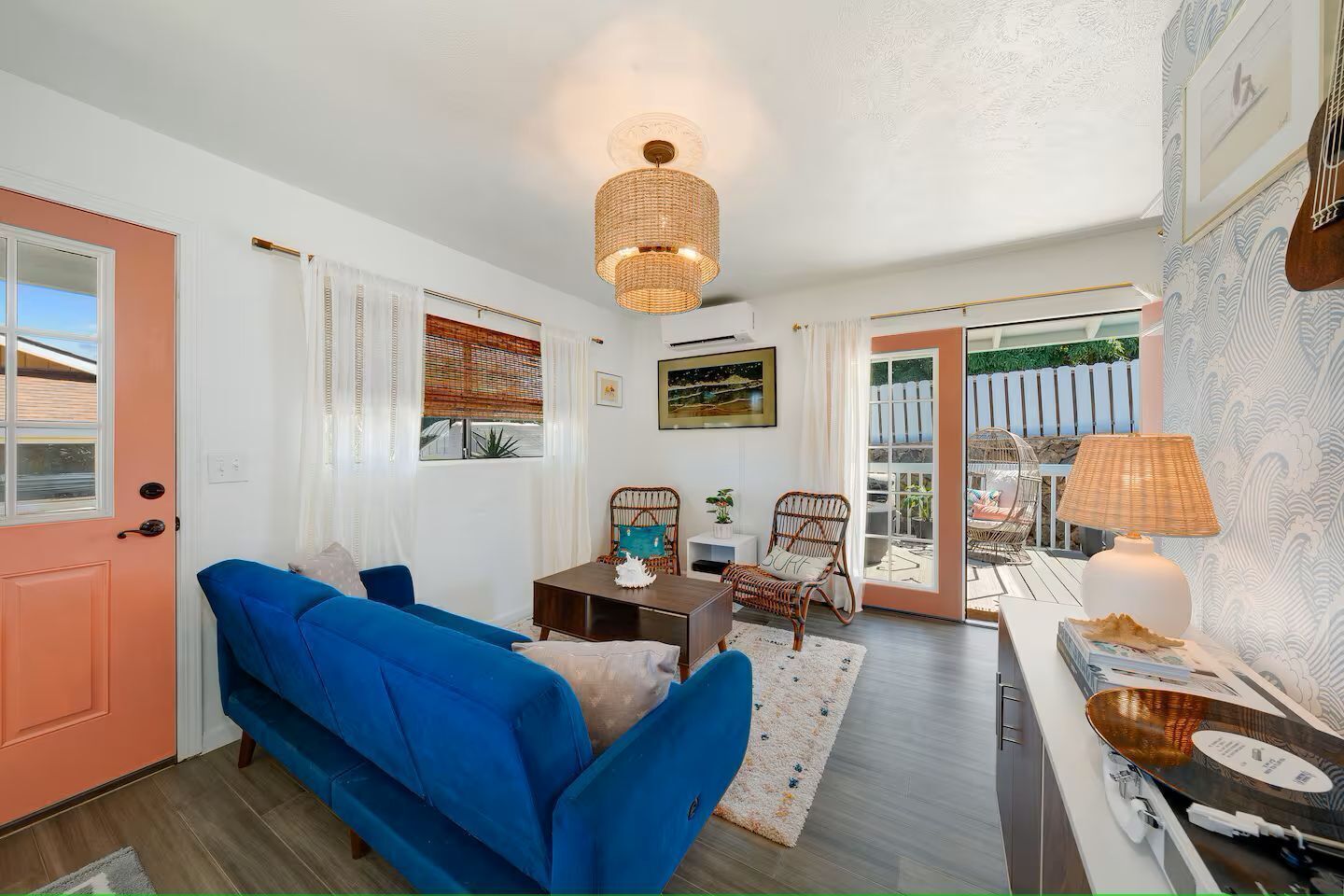 Un salon chaleureux avec un canapé bleu, des fauteuils en osier, une petite table et une lampe.