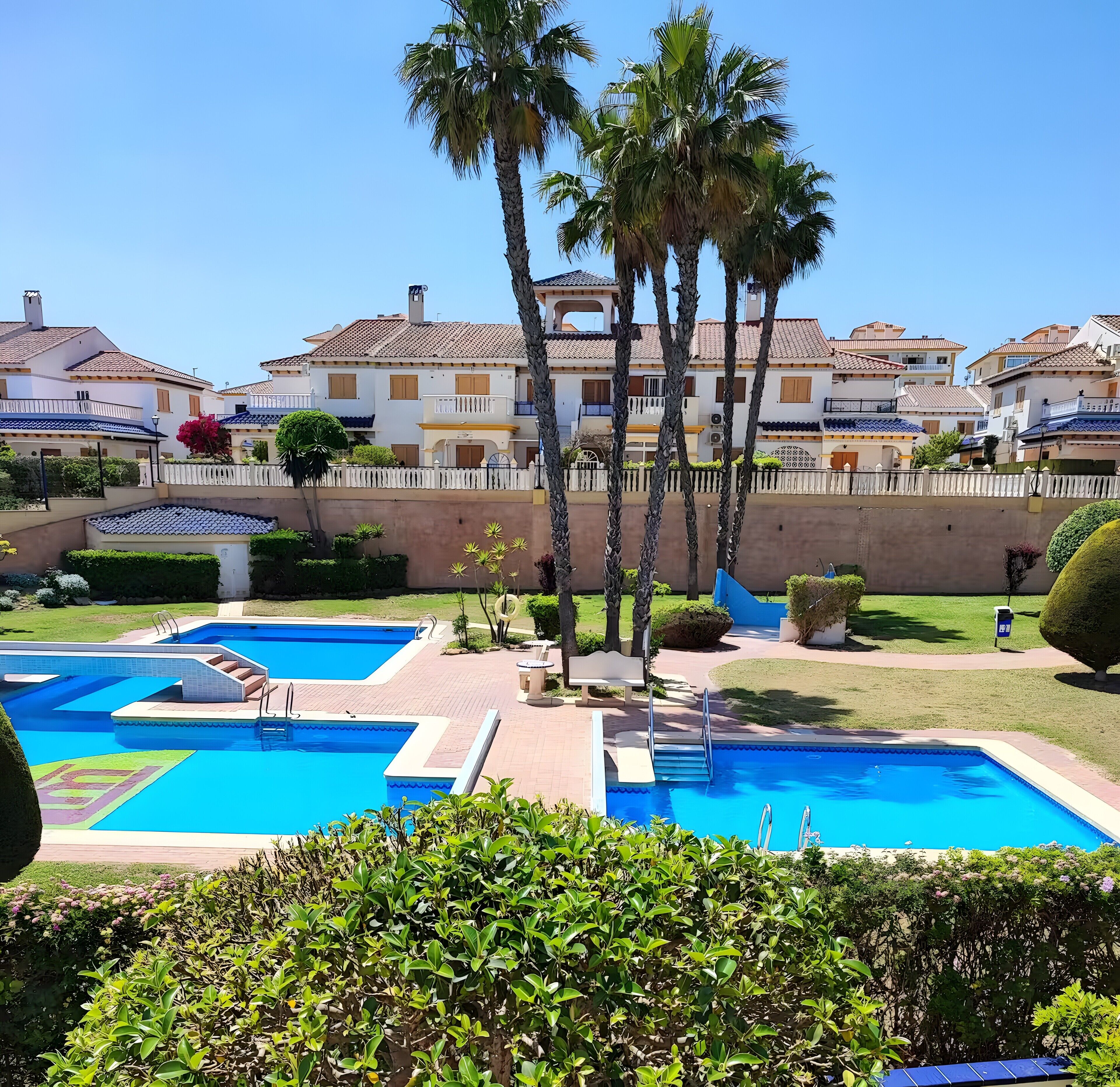 A pool area with steps leading into the water, surrounded by palm trees and a white fence.