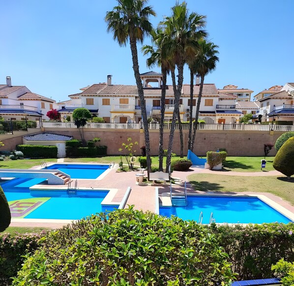 Zona de piscina con escalones que bajan al agua, rodeada de palmeras y una valla blanca.
