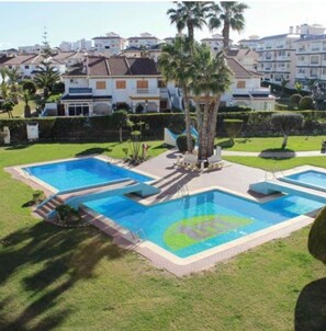 A residential area with a swimming pool complex, palm trees, and a building in the background.
