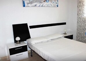 Un dormitorio con cama, mesita de noche, lámpara y un cuadro colgado en la pared.