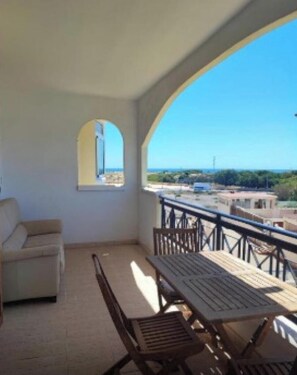 Un balcón con mesa y sillas, un sofá y vistas al mar y edificios.