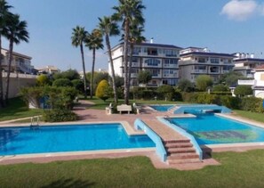 Un hotel con varias piscinas, palmeras y un césped bien cuidado.