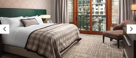 A hotel room with a large bed, a chair, a nightstand, and a view of a building through a glass door.