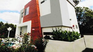 Ein modernes, zweistöckiges Haus mit roter und weißer Fassade, umgeben von üppigem Grün und blauem Himmel.