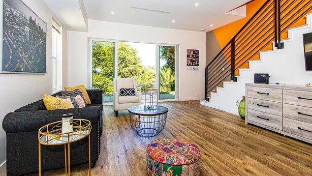 Ein modernes Wohnzimmer mit Sofa, Couchtisch und Sesseln, einer Treppe mit orangefarbenen Akzenten sowie Blick durch Glastüren.