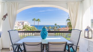 A balcony with a table and chairs, a decorative vase, and a view of the sea and buildings. - ‘Frente Al Mar Mijas’ Apartment with Sea Views, Shared Pool and Wi-Fi (Mijas costa)