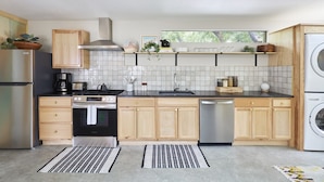 A modern kitchen with wooden cabinets, a stainless steel stove, a dishwasher, and a window above the sink. - La Dea Santa Fe - Entire 6 Suite Compound (Santa Fe)