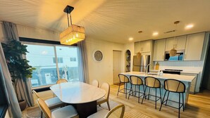 A modern kitchen with a central island, a dining area with a round table and chairs, and a large window providing a view of the outside.