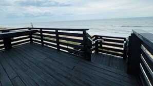A wooden deck with a railing overlooking a beach.