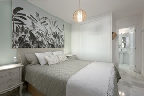 Une chambre à coucher comprenant un lit, une table de chevet, un luminaire fixé au mur, et une salle de bain visible à travers une porte ouverte.