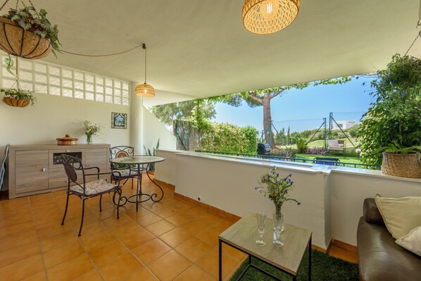 Un balcon donnant sur un espace verdoyant et un bâtiment, un coin repas avec une table et des chaises, et un canapé.