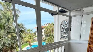 A room with large windows, a tiled floor, and a view of a swimming pool and palm trees. - Apartment 'Con Piscina' with Shared Pool, Wi-Fi and Air Conditioning (La Mata)