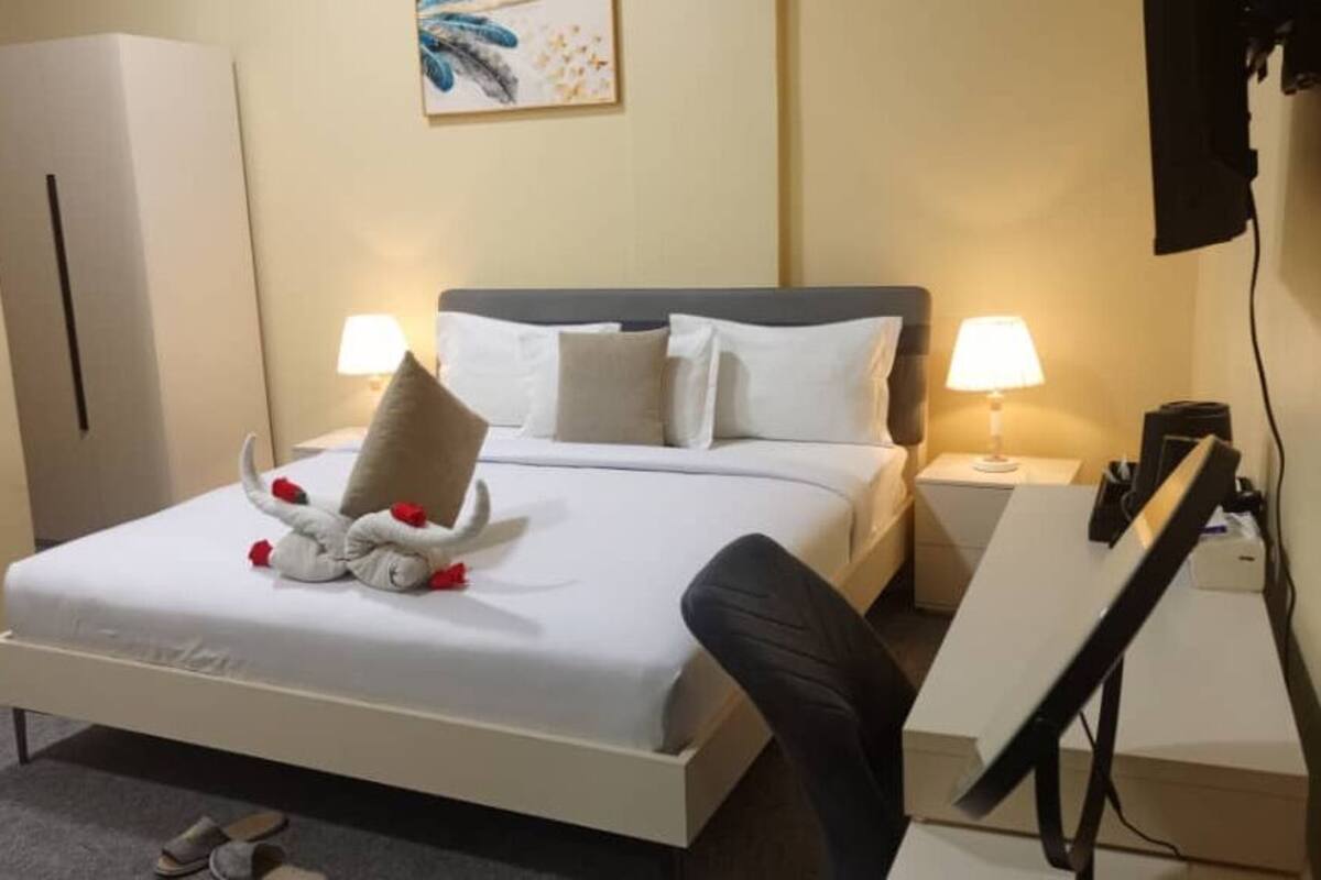 Una habitación de hotel con cama, dos lámparas de noche, un escritorio con silla, un televisor de pantalla plana y un cuadro en la pared.