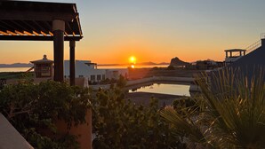 Une vue sur le coucher de soleil depuis une terrasse avec piscine, donnant sur une étendue d’eau et des montagnes lointaines.