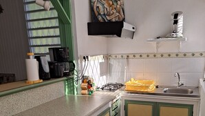 Una cocina con gabinetes verdes, una tabla de cortar de madera, una estufa a gas, un fregadero y un cuadro en la pared.