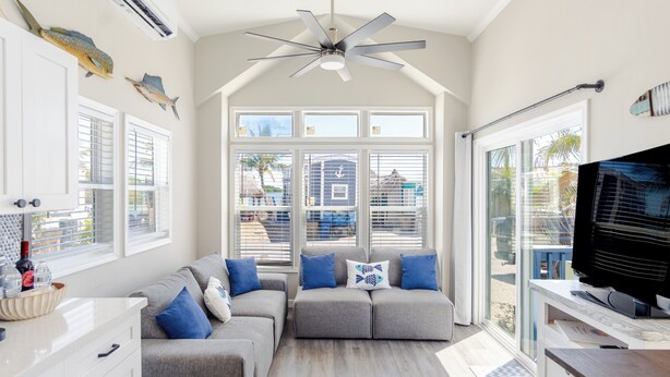 A spacious living room with a grey sectional sofa, a flat-screen TV, and a ceiling fan. - Little Piece of Paradise /w Kayaks, Private Dock and BBQ (Key Largo)