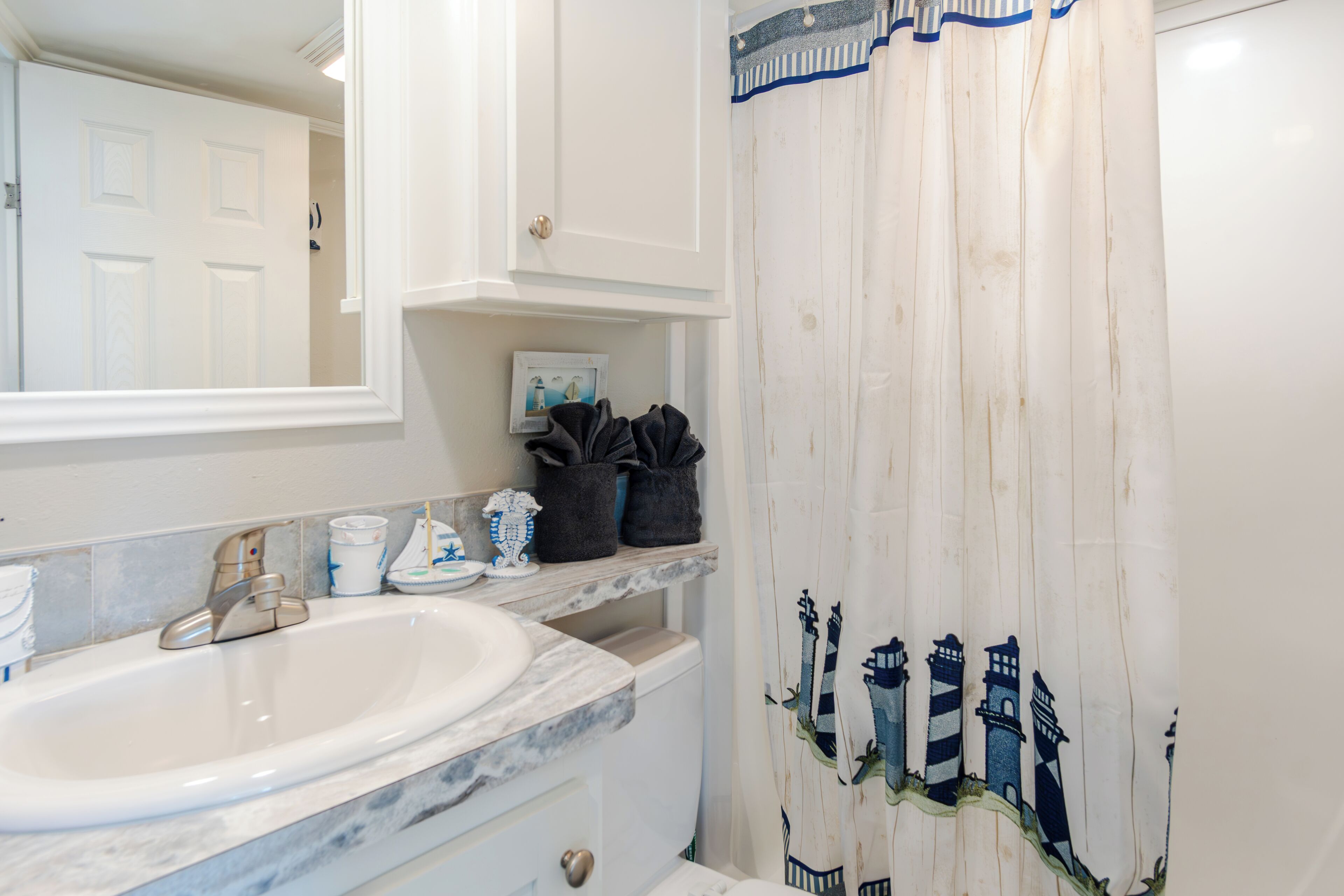 A bathroom with a white sink, a mirror, a towel rack, and a shower curtain with a lighthouse design.