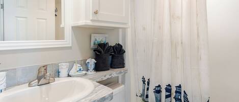 A bathroom with a white sink, a mirror, a towel rack, and a shower curtain with a lighthouse design.
