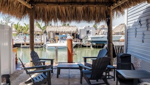 A covered outdoor seating area with chairs and tables, overlooking a marina with boats. - Little Piece of Paradise /w Kayaks, Private Dock and BBQ (Key Largo)