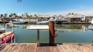 A wooden dock with a table and a trash bin, boats docked in the background, and thatched-roof structures. - Little Piece of Paradise /w Kayaks, Private Dock and BBQ (Key Largo)