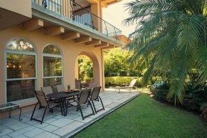 A patio with a table and chairs, a covered seating area, and a view of a lush garden with palm trees. - Bella Vista 7E, 3Bdr/3.5 Bth Condo (Playa Herradura)