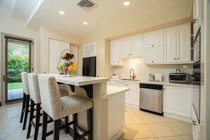 Una cocina con armarios blancos, una isla central, un refrigerador, un lavavajillas y un tostador.
