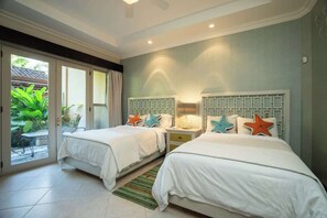 Habitación de hotel con dos camas, una puerta corrediza de vidrio al exterior y una pequeña mesa con sillas.
