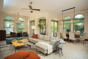 A spacious living area with a sofa, coffee table, and dining table, large windows with blinds, and a ceiling fan. - Bella Vista 7E, 3Bdr/3.5 Bth Condo (Playa Herradura)