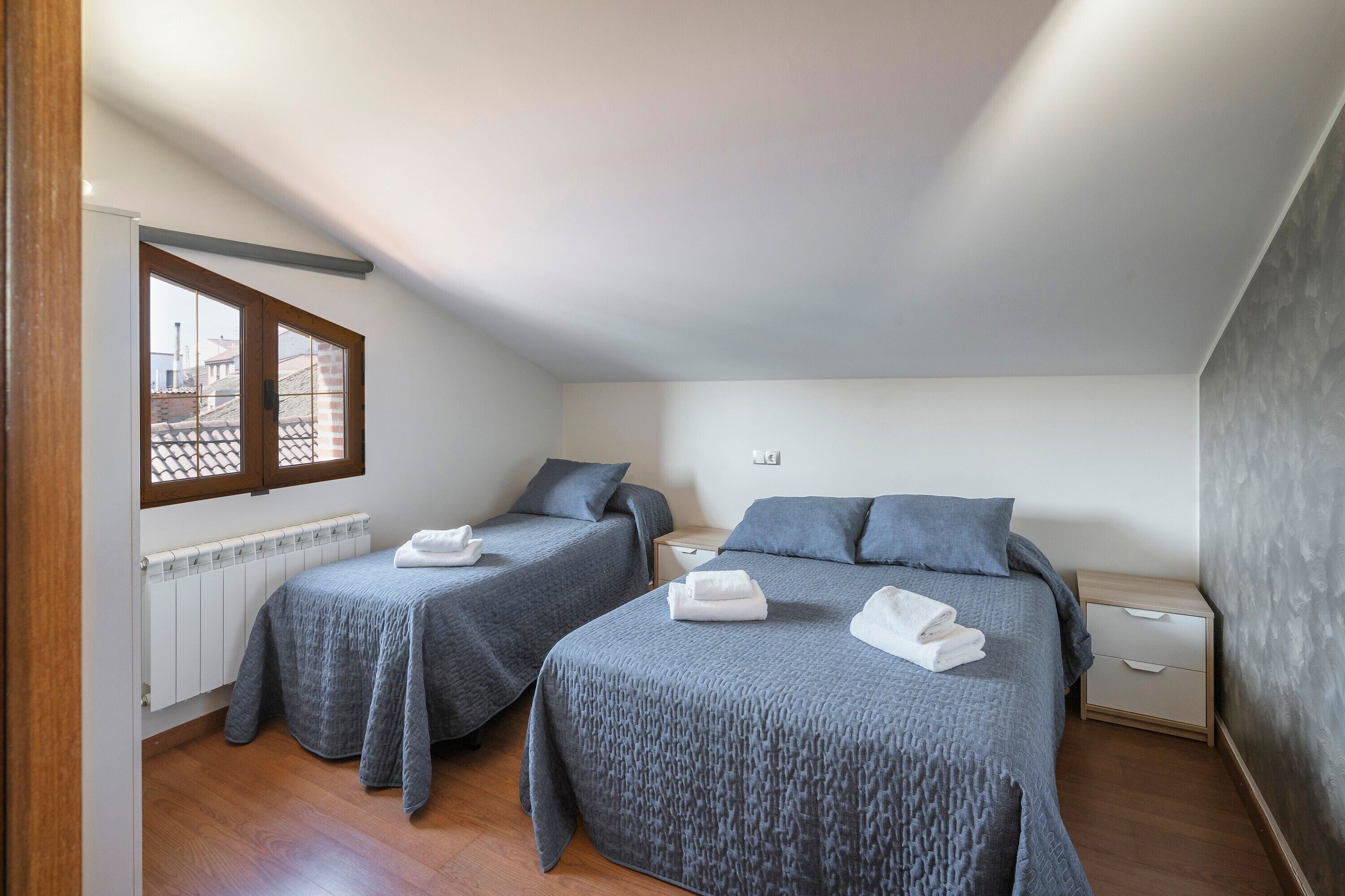 Un dormitorio con dos camas, una ventana, un radiador y una mesita de noche.