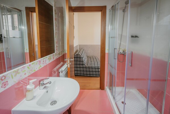 Un baño con lavamanos, espejo, ducha y alfombra de baño estampada.