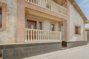 A building with a brick facade, a balcony with balustrades, and a tiled ground floor. - Rural House Los Alisos with Private Pool and Terrace in Coca, Segovia (Coca)
