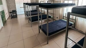 A dormitory room with bunk beds, a small table, and a chair.