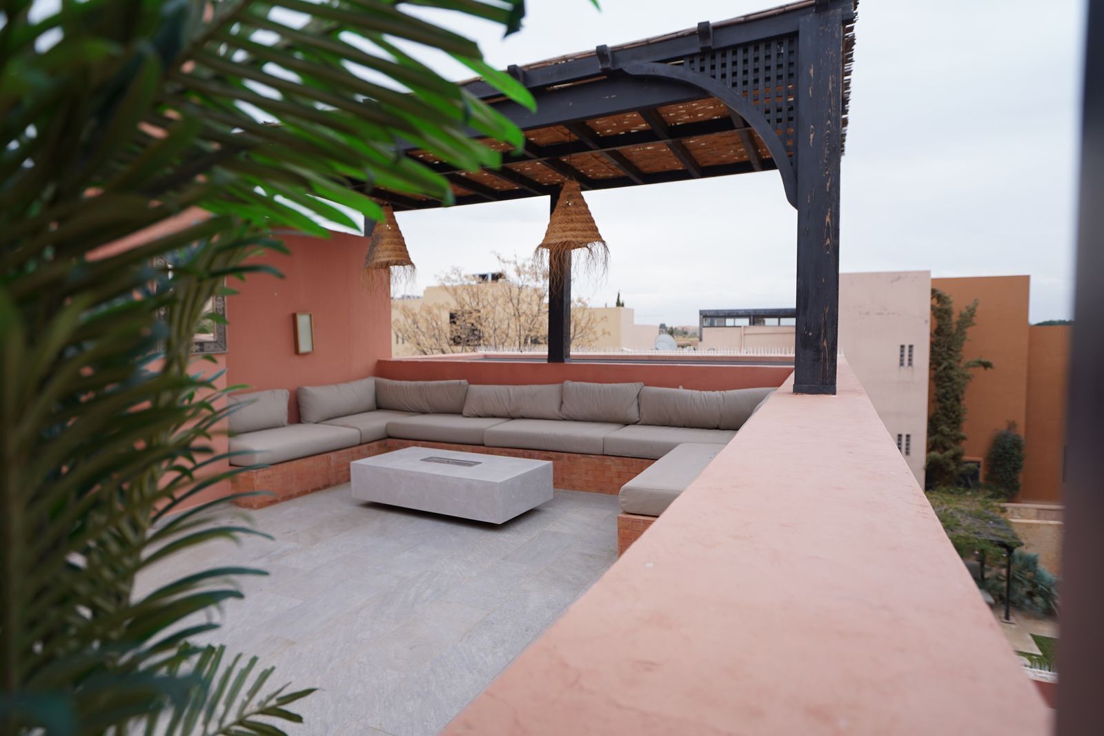 Un espacio exterior moderno con una mesa de centro de piedra, un sofá acolchado y una estructura de pérgola.