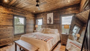 A wooden cabin bedroom with a large bed, a wooden bench, two nightstands, and a ceiling fan. - Get away and relax at Elk Ridge, a modern lodge in the mountains of Ruidoso. (Ruidoso)