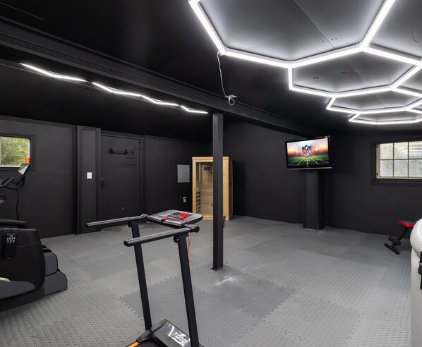 Et fitnesscenter med træningsudstyr, et løbebånd og et fjernsyn, der viser NFL-logoet.