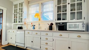 Una cucina con mobili bianchi, un forno a microonde, una macchina del caffè e una finestra con persiane.