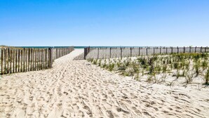 Ein Sandweg am Strand, gesäumt von einem hölzernen Zaun auf beiden Seiten, der zum Meer führt.