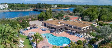 An aerial view of a resort with a swimming pool, lounge chairs, and a tennis court.