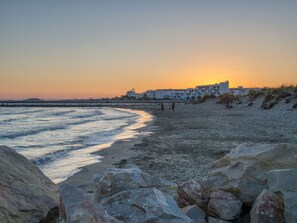 A beach with rocky foreground, waves, and buildings in the background. - Sowell Résidence Les Sablons by Interhome (Le Grau du Roi)