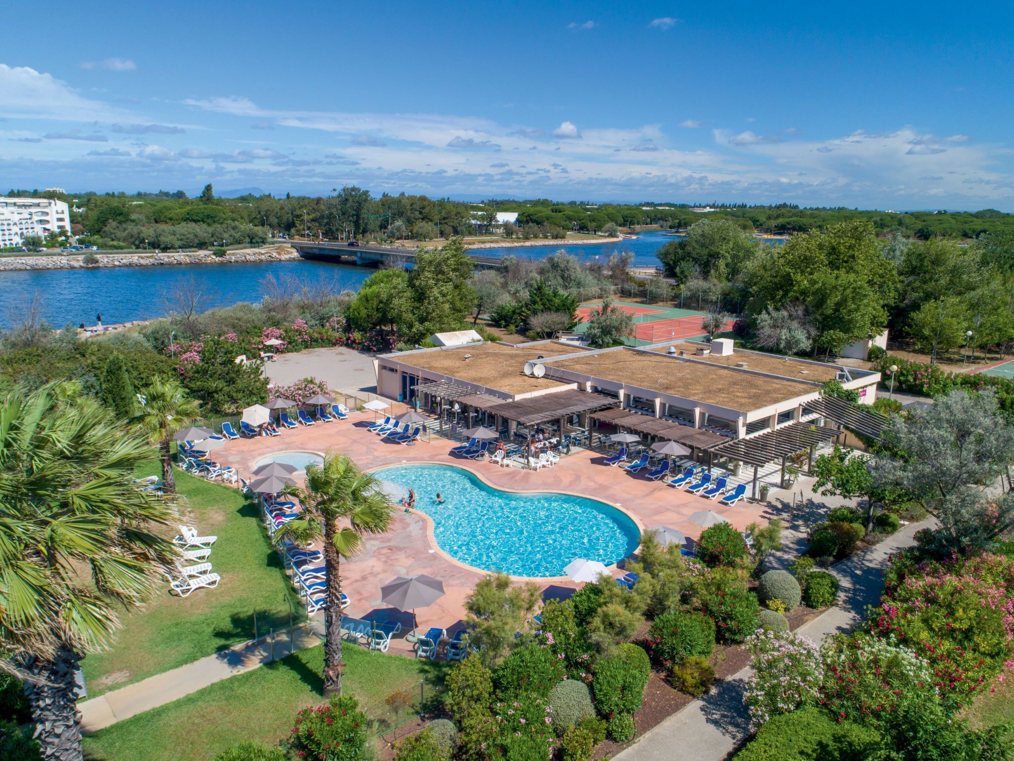 Vista aerea di un resort con piscina, poltrone da relax e campo da tennis.