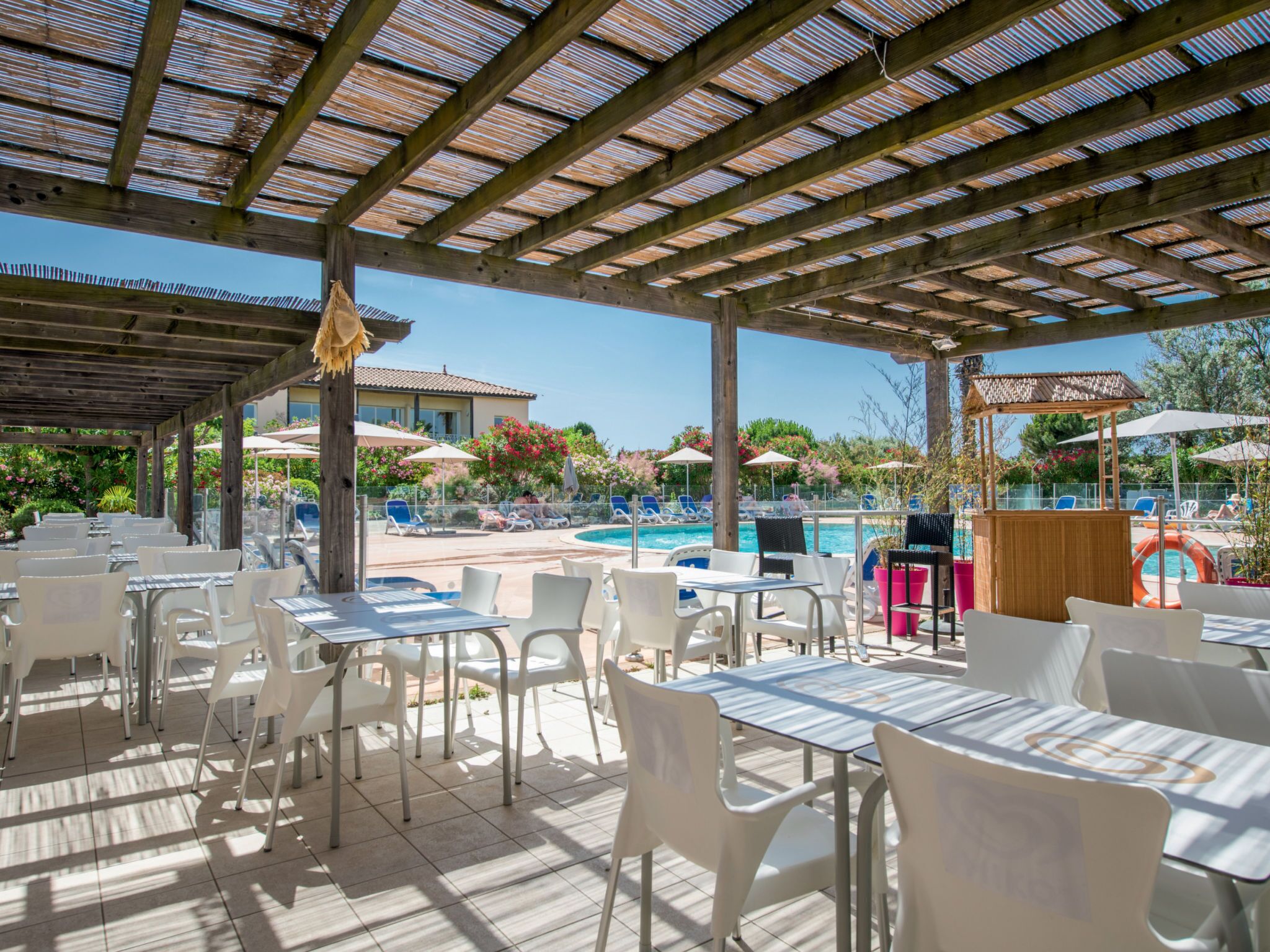 Een buitenterras met tafels, stoelen, een zwembad en parasols.