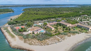 An aerial view of a coastal resort with a beach, tennis courts, and a large building with multiple rooms.